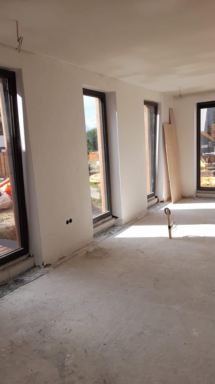 Strak pleisterwerk rond hoge zwarte kozijnen in een nieuwbouwwoning